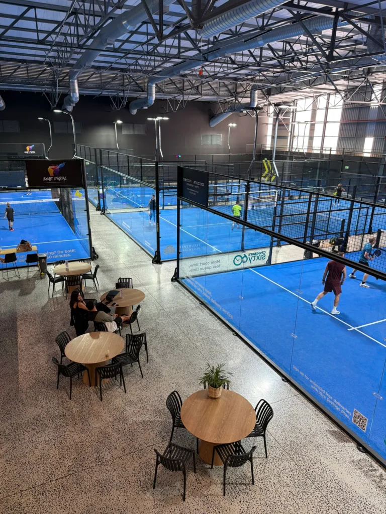 Café tables beside the glass-walled courts at PadelX Somerset West