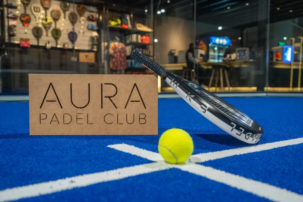 Aura Padel Club sign with a racket and ball on court, pro shop behind