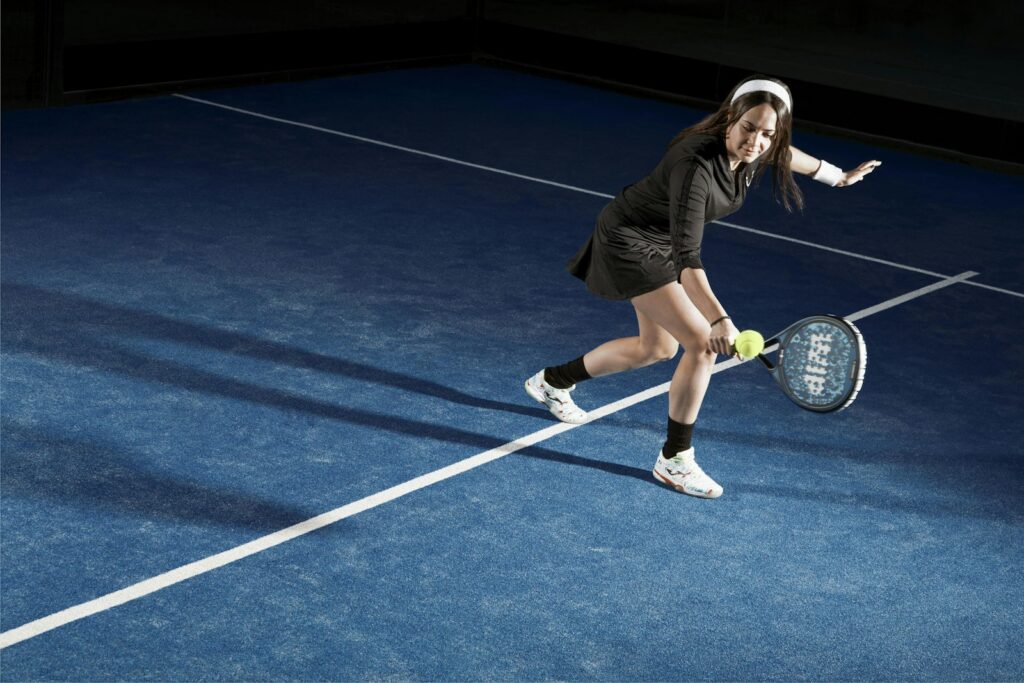 Female padel player stretching low for a volley on a blue padel court