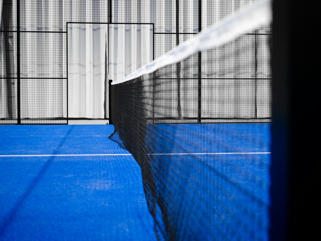Padel net on a blue artificial grass court with glass and mesh walls