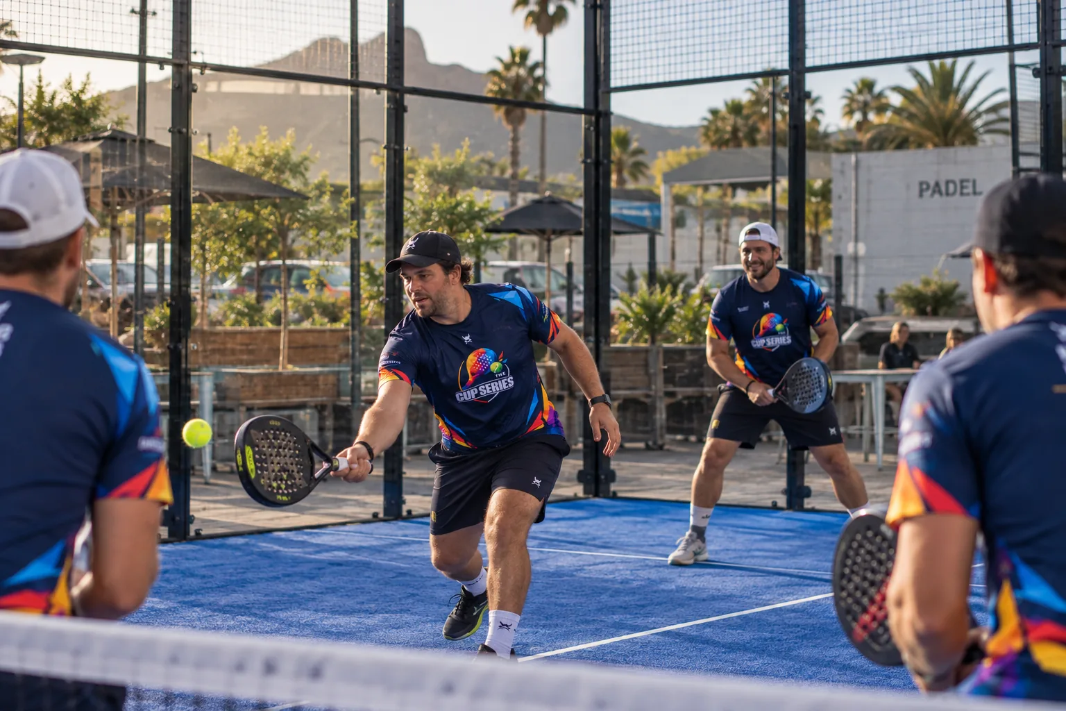 Men's padel doubles in Cup Series shirts, one player volleying while his partner waits