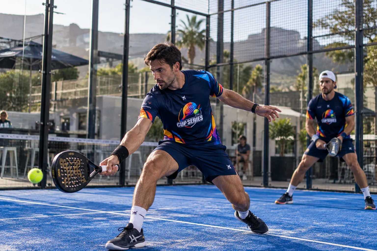 Padel player in a Cup Series shirt reaching for a low ball, with Table Mountain behind the court